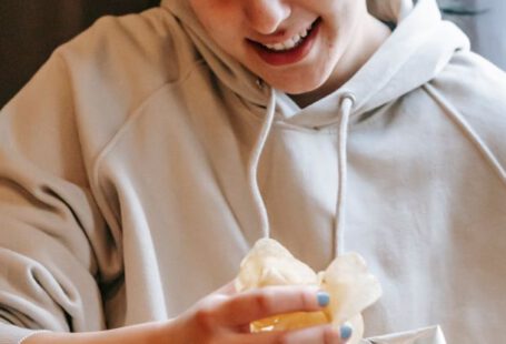 Shareable Content - Smiling plump female wearing comfy hoodie eating crispy yummy potato chips while sitting in light room